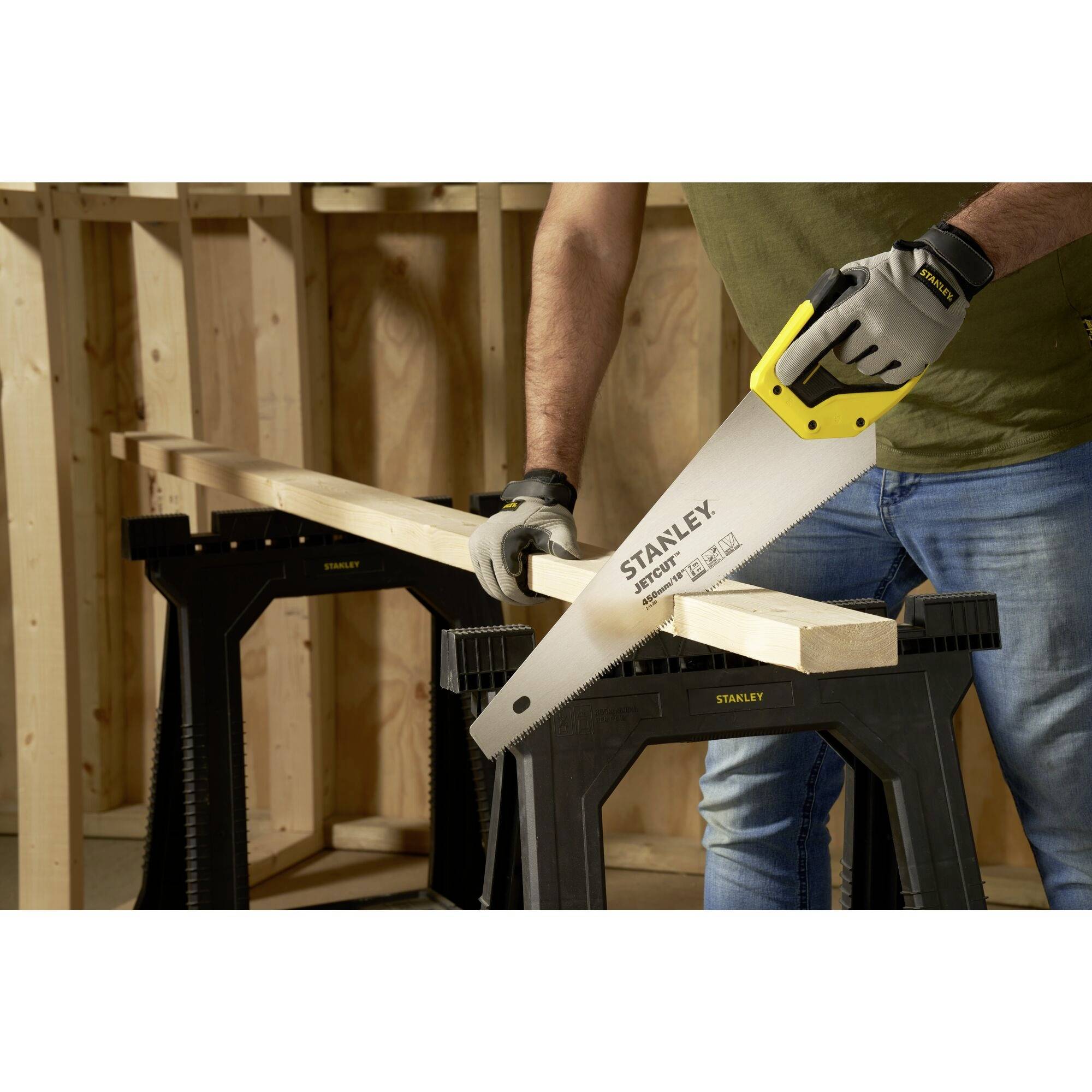 A person is cutting a piece of wood with a handsaw, which is resting on sawhorses. The saw and tools are made by Stanley.
