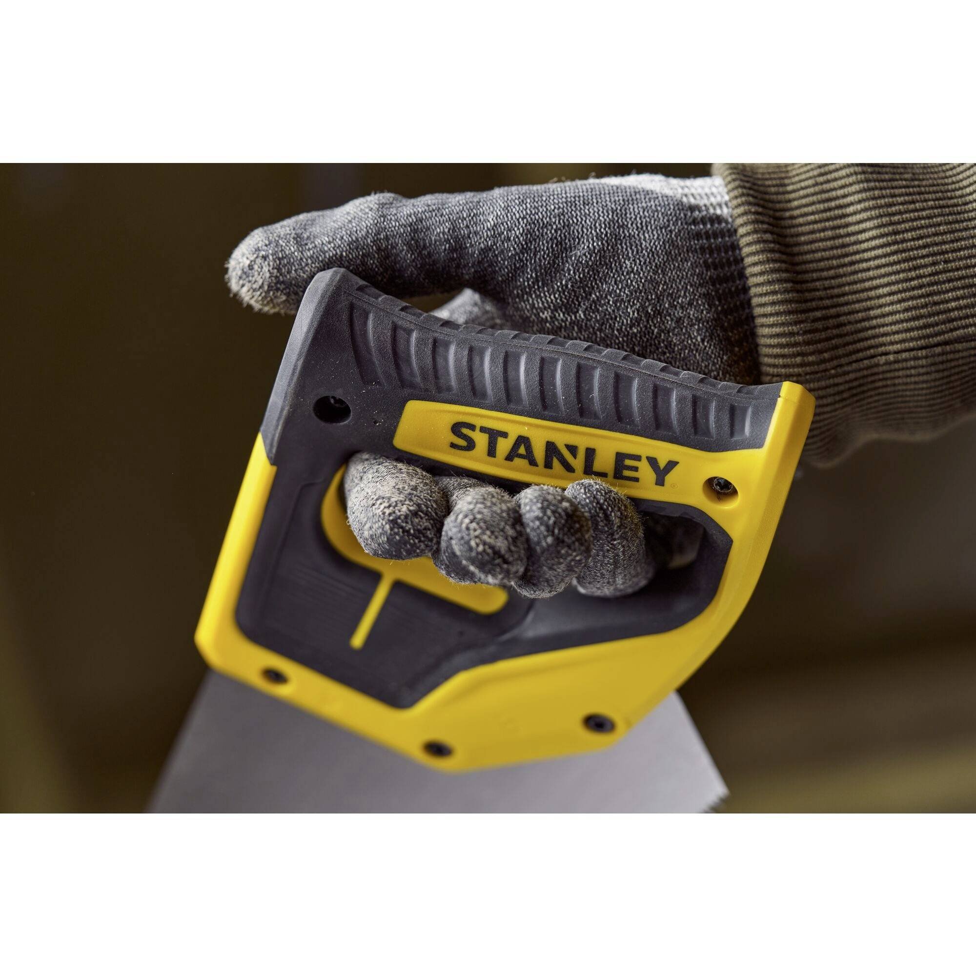 A hand wearing a work glove is gripping a yellow tool handle of a saw with the inscription 'STANLEY'.