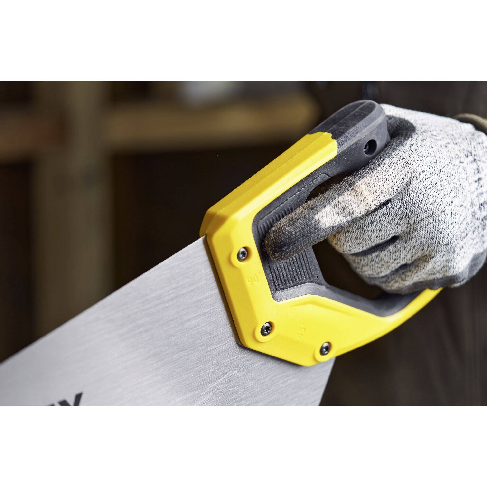 A hand wearing a glove is holding a yellow and black handsaw. The focus is on the saw's handle.