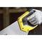 A hand wearing a glove is holding a yellow and black handsaw. The focus is on the saw's handle.