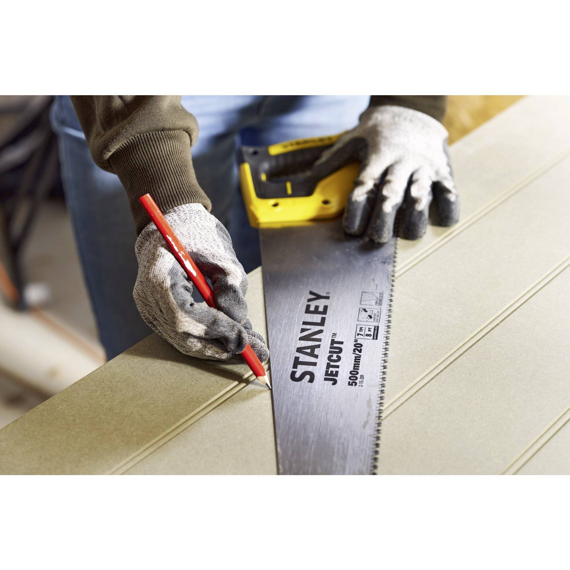 A person is holding a handsaw and marking a cutting point on a wooden board with a red pen.