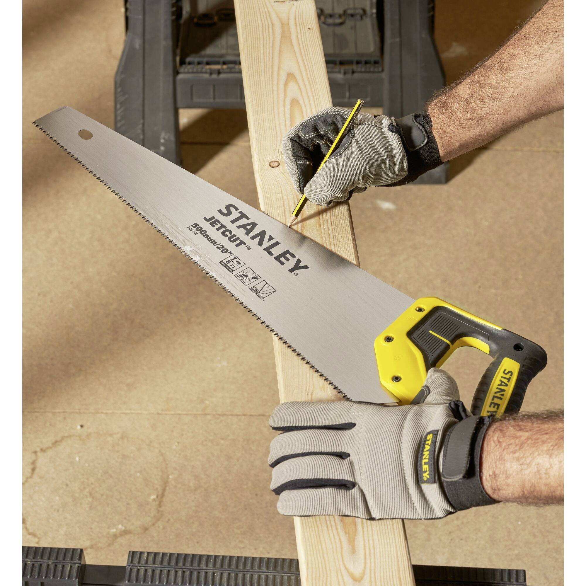 A person is marking a wooden board with a pencil while supporting it with a handsaw. Gloves provide protection.