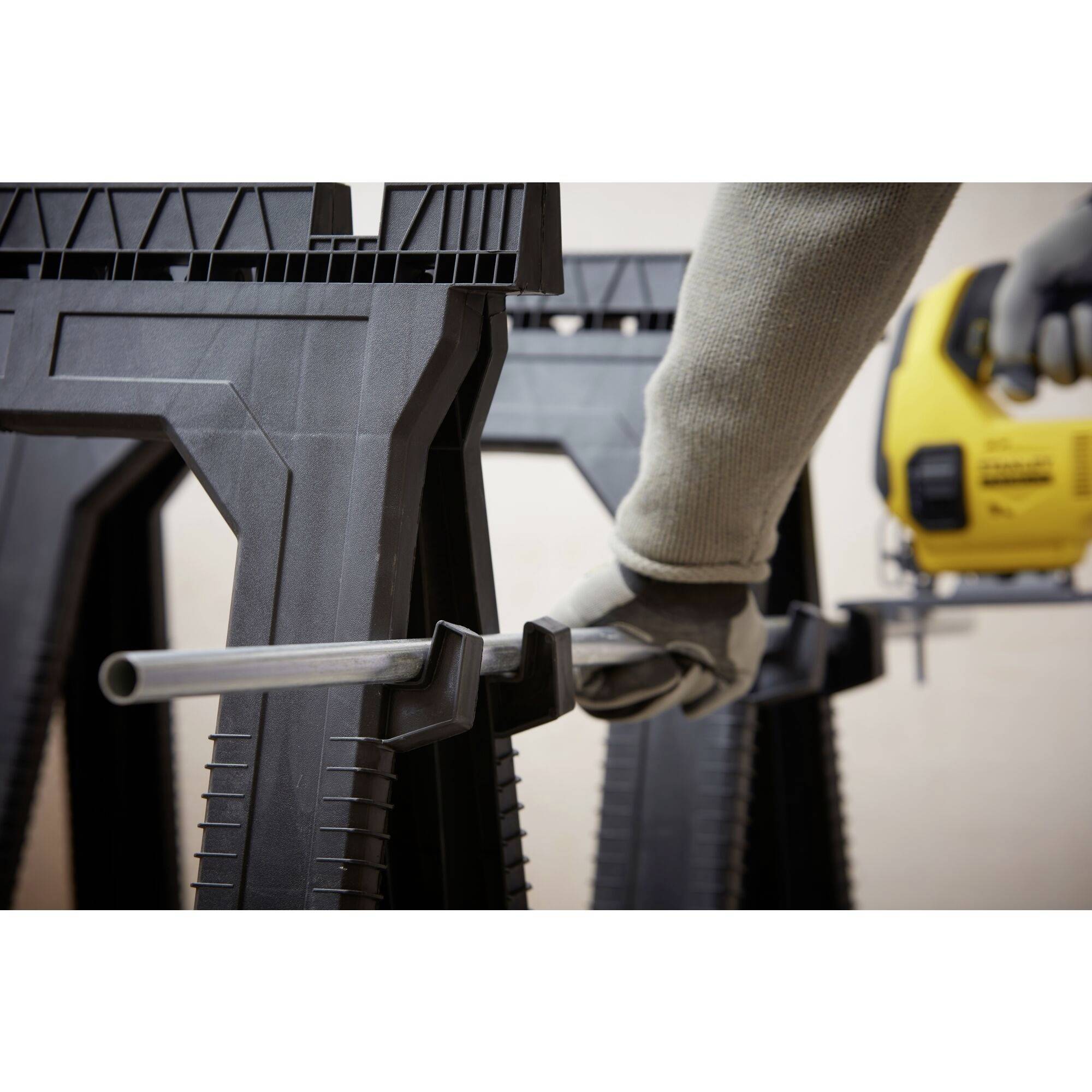 A person is cutting a metal pipe with an electric saw. The scene depicts a workshop with a yellow tool in hand.