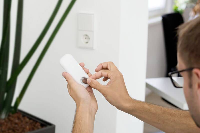 A person is changing the batteries in a remote control. A green plant is in the background.