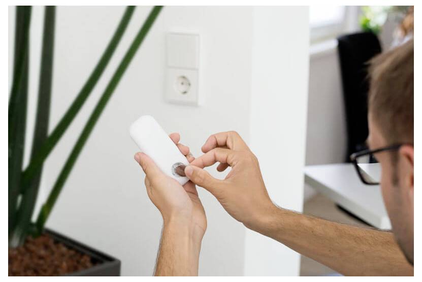 Person using a small white plug-in device, likely a night light or sensor, by adjusting a dial near a wall outlet.