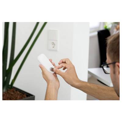 Person using a small white plug-in device, likely a night light or sensor, by adjusting a dial near a wall outlet.