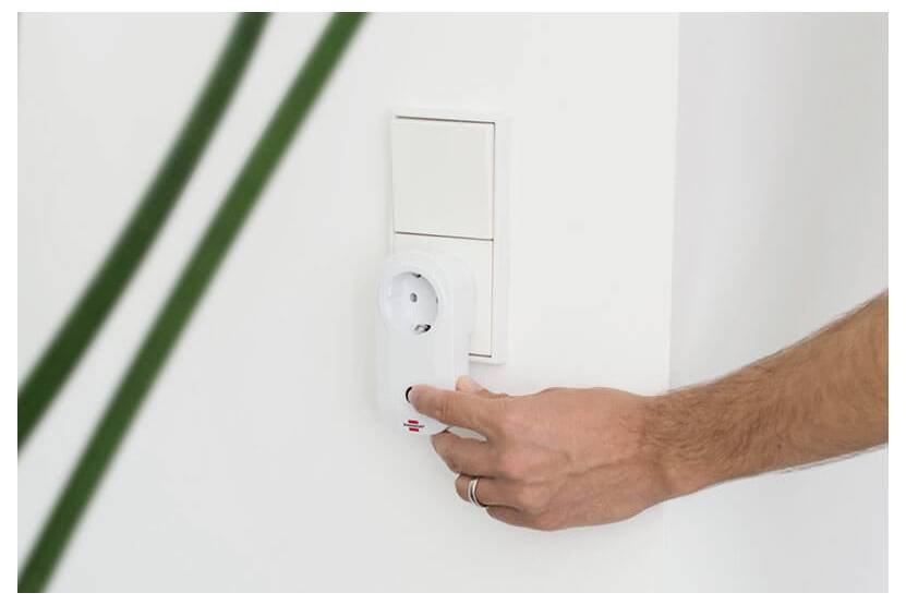 Hand turning a wall-mounted thermostat or control knob on a white wall.