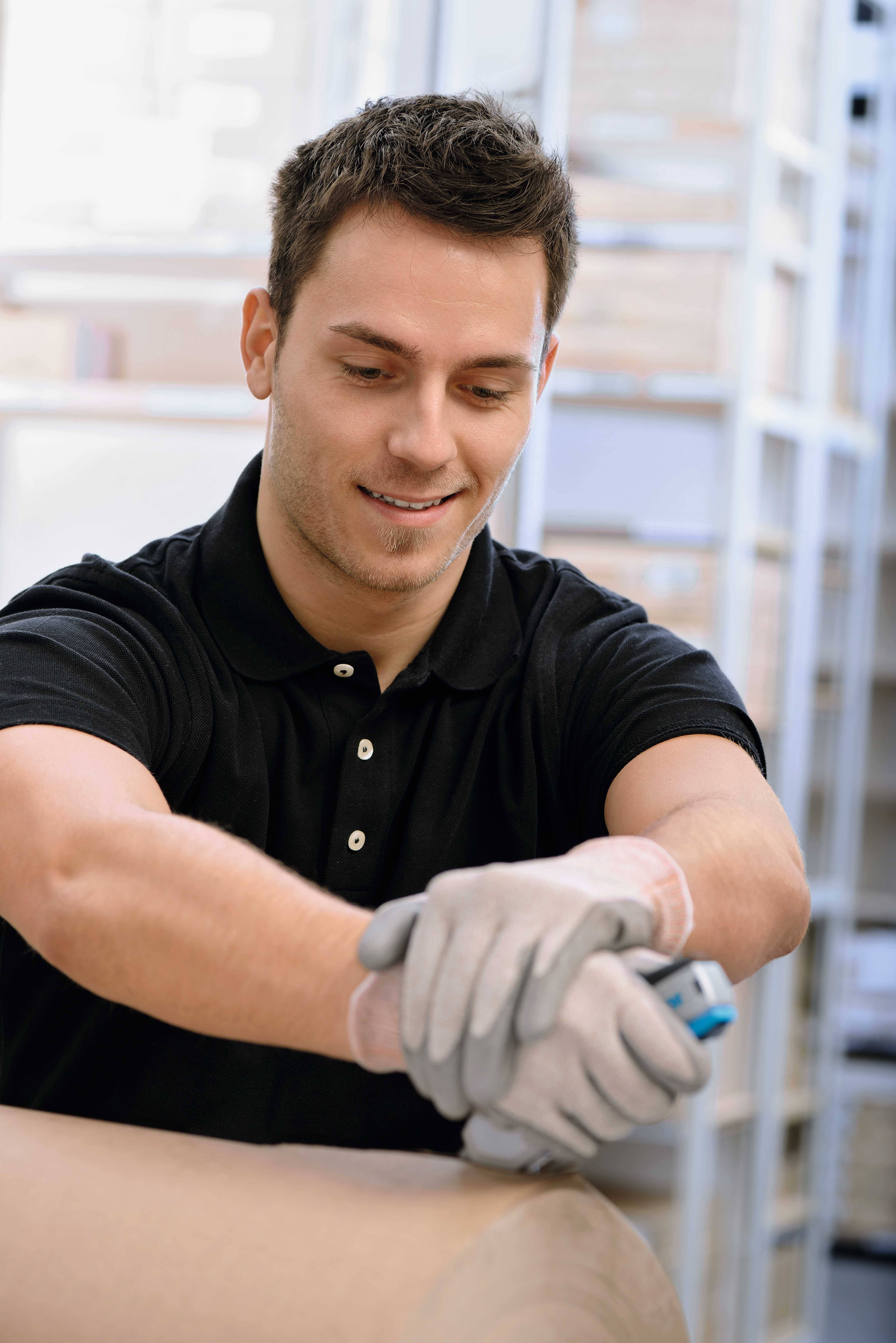 A man in a black polo shirt and gloves is carefully working on a large roll with a tool in his hand.