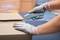 A person wearing gloves carefully opens a cardboard box containing a grey cutting tool. Background out of focus.
