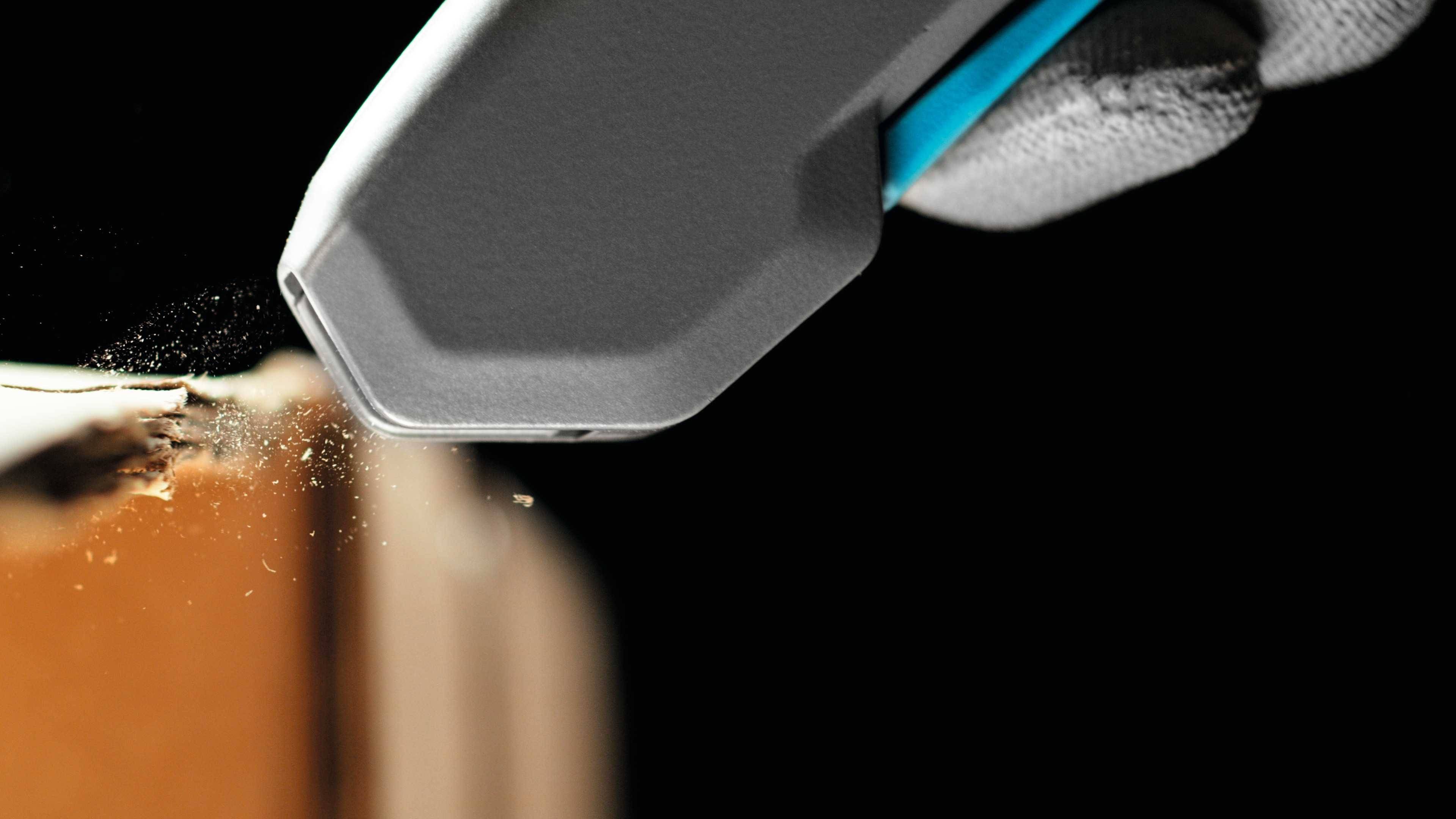 A craft knife cuts precisely into a cardboard box. In the background, a black, high-contrast background is visible.