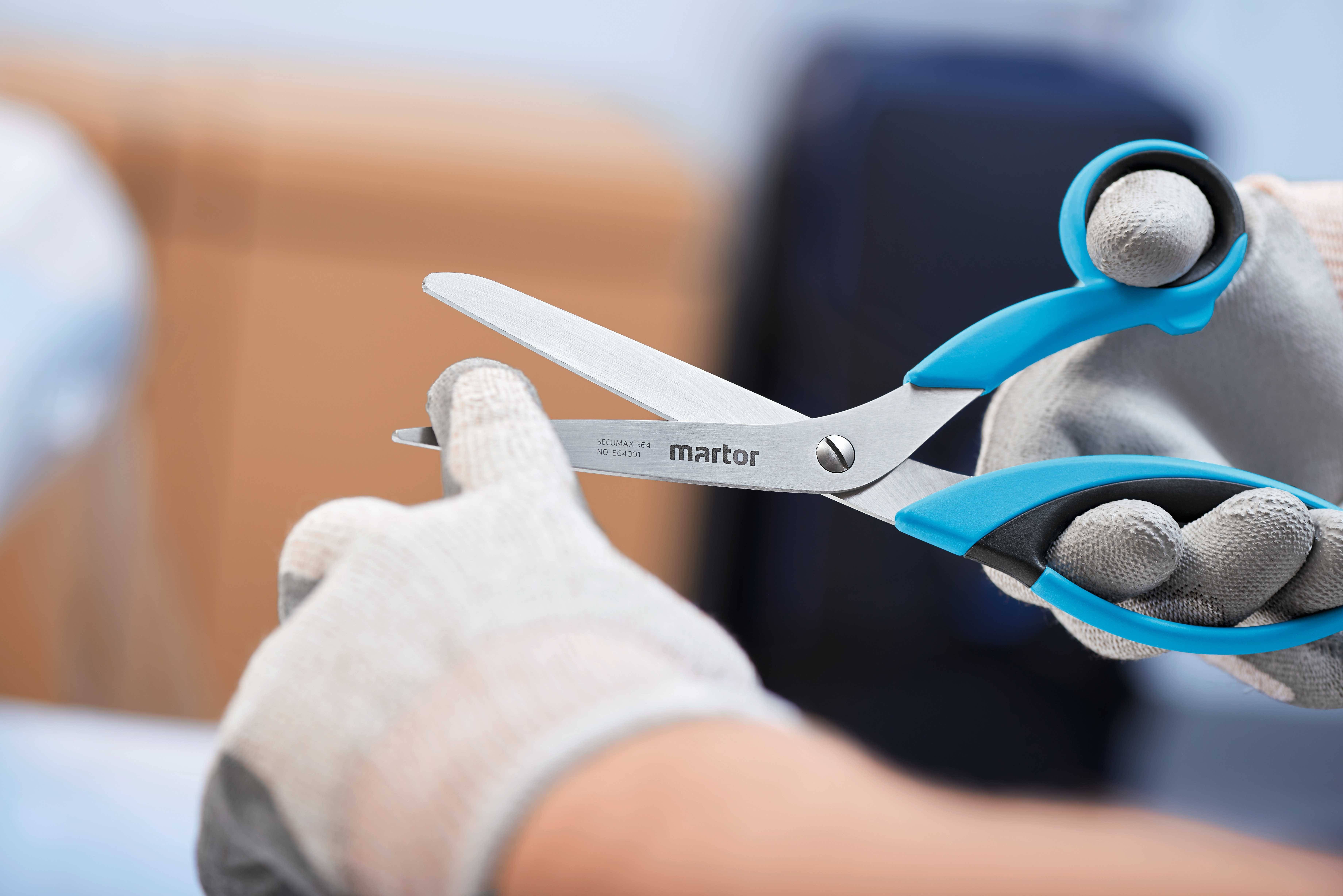 A person is wearing gloves and holding a Martor safety scissors, ready to cut.