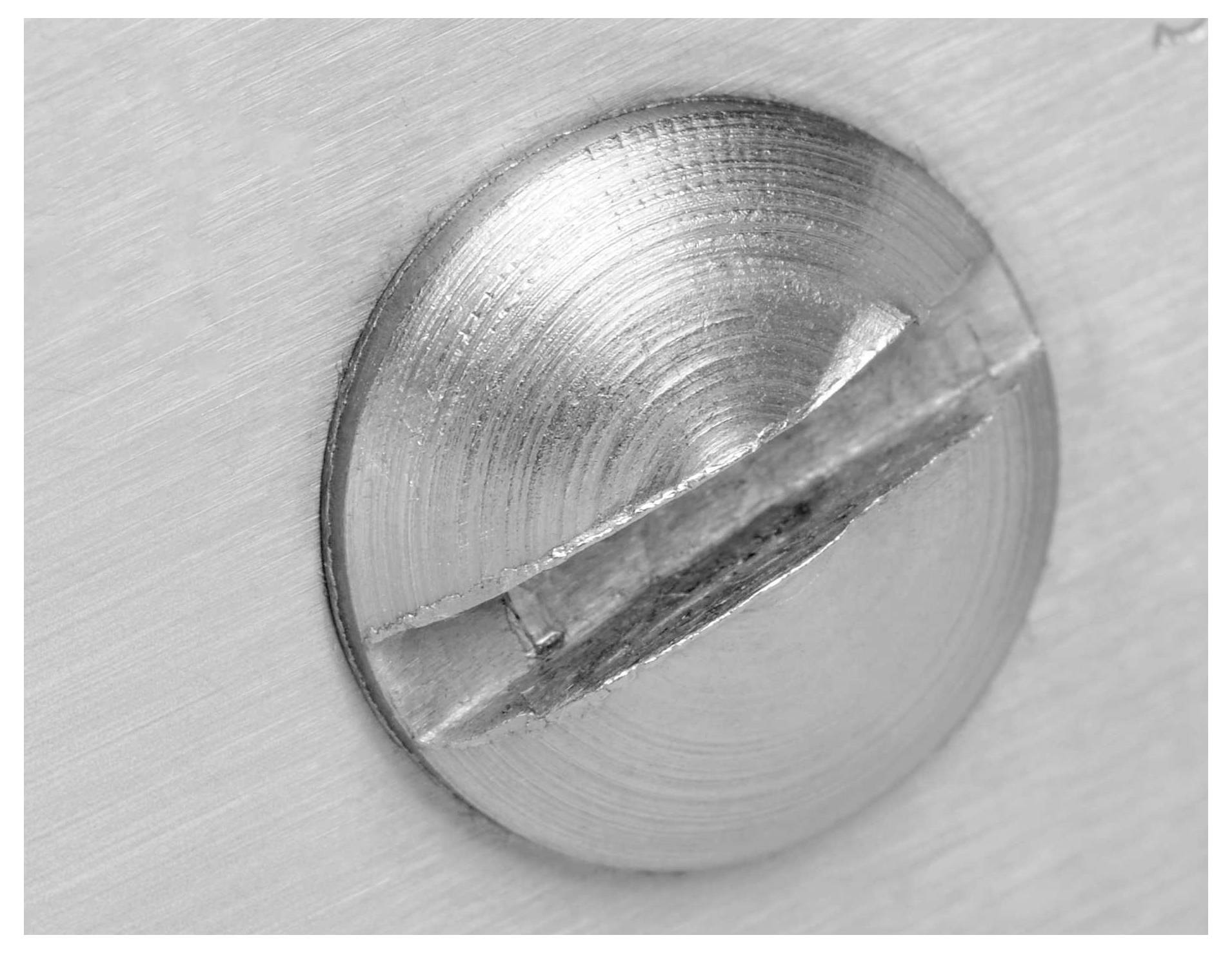 Close-up of a silver, flat-headed screw being screwed into a smooth surface.