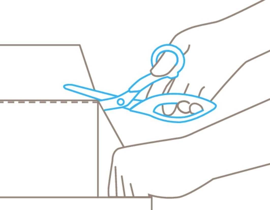 A hand is using scissors to cut a cardboard box along the dotted line.