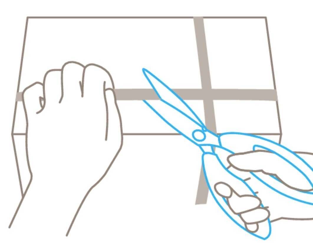 A hand carefully holds scissors and cuts through the packing tape on a cardboard box.