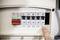 A finger points at an electrical fuse box with multiple switches numbered from 1 to 5. The main switch is turned off.
