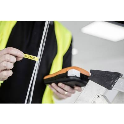 A person wearing a high-visibility yellow vest is holding an orange and black device and a yellow labelling strip next to a ladder.
