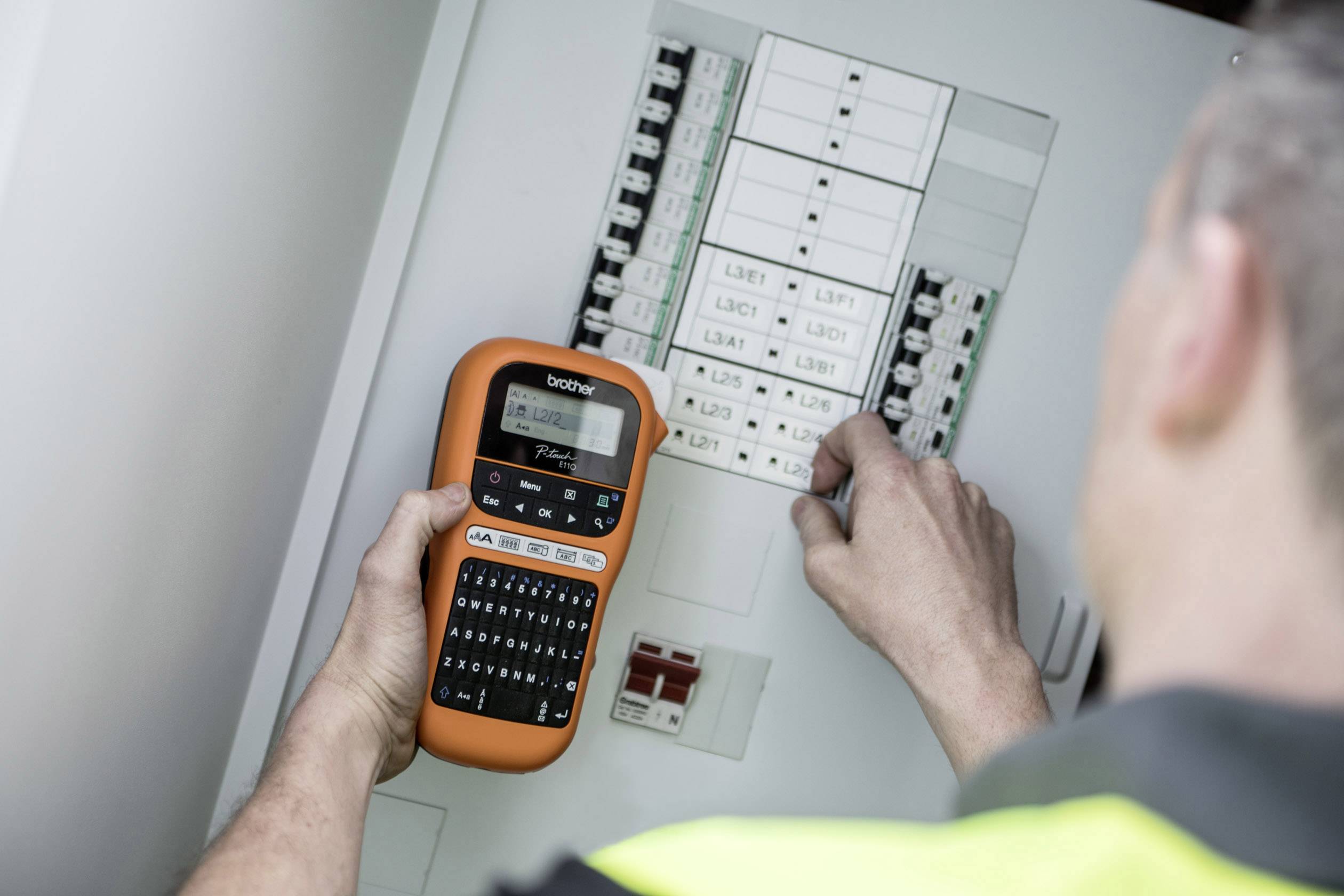 A person is using a labelling device to organise signs on an electrical cabinet. The focus is on precise labelling.