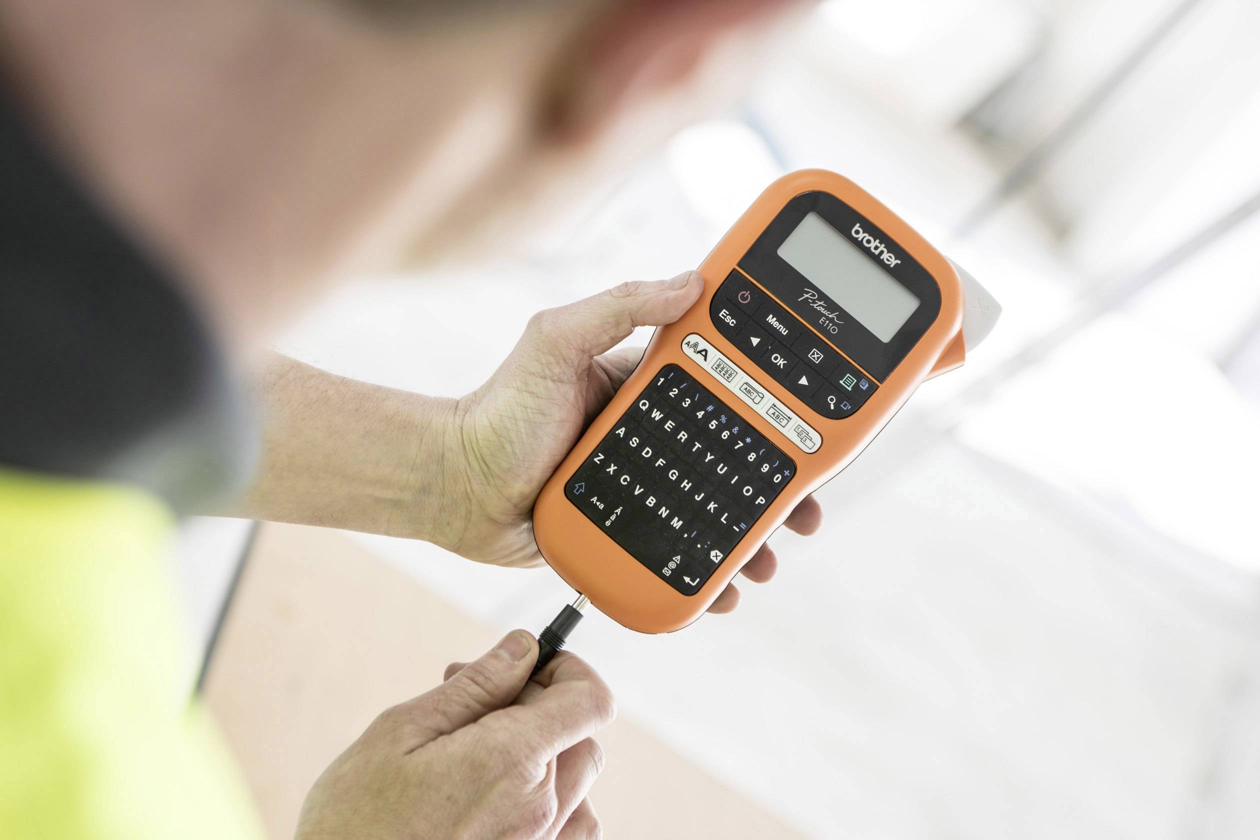 A person is holding an orange Brother labelling device and inputting text while using it with both hands.