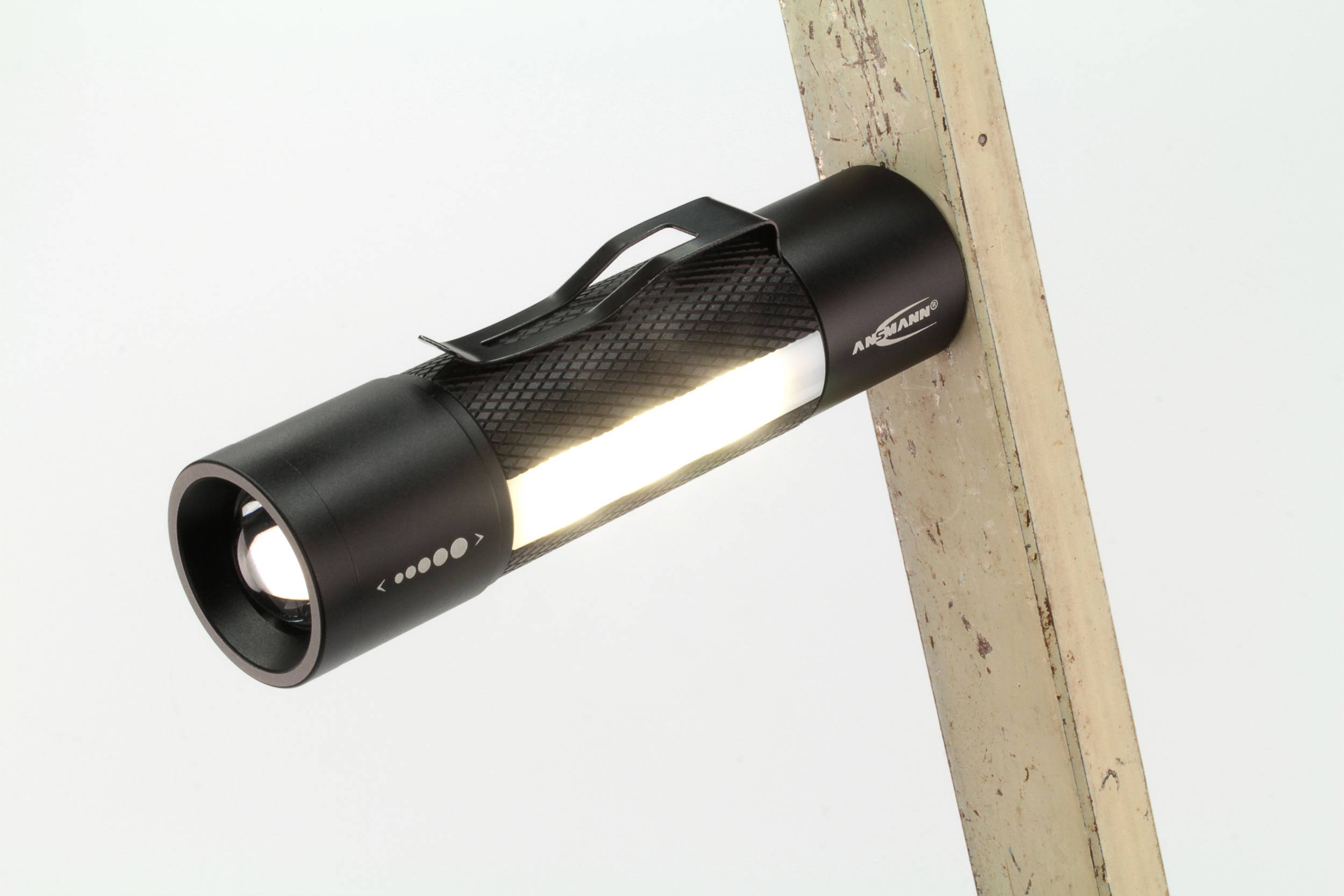 A black torch with illuminating light, attached to an angled piece of wood. It has a non-slip surface.