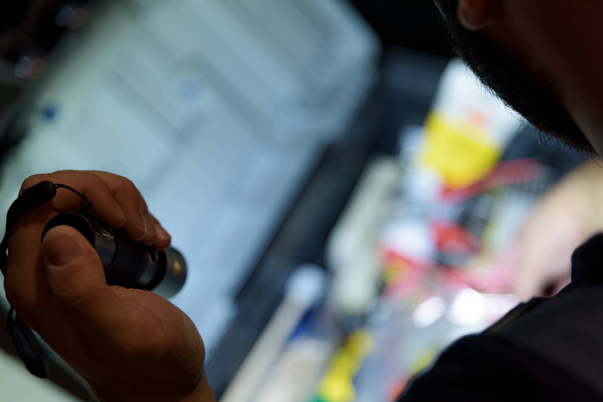 A person is holding a torch in a dark room, while pointing towards a blurry background with cables and equipment.