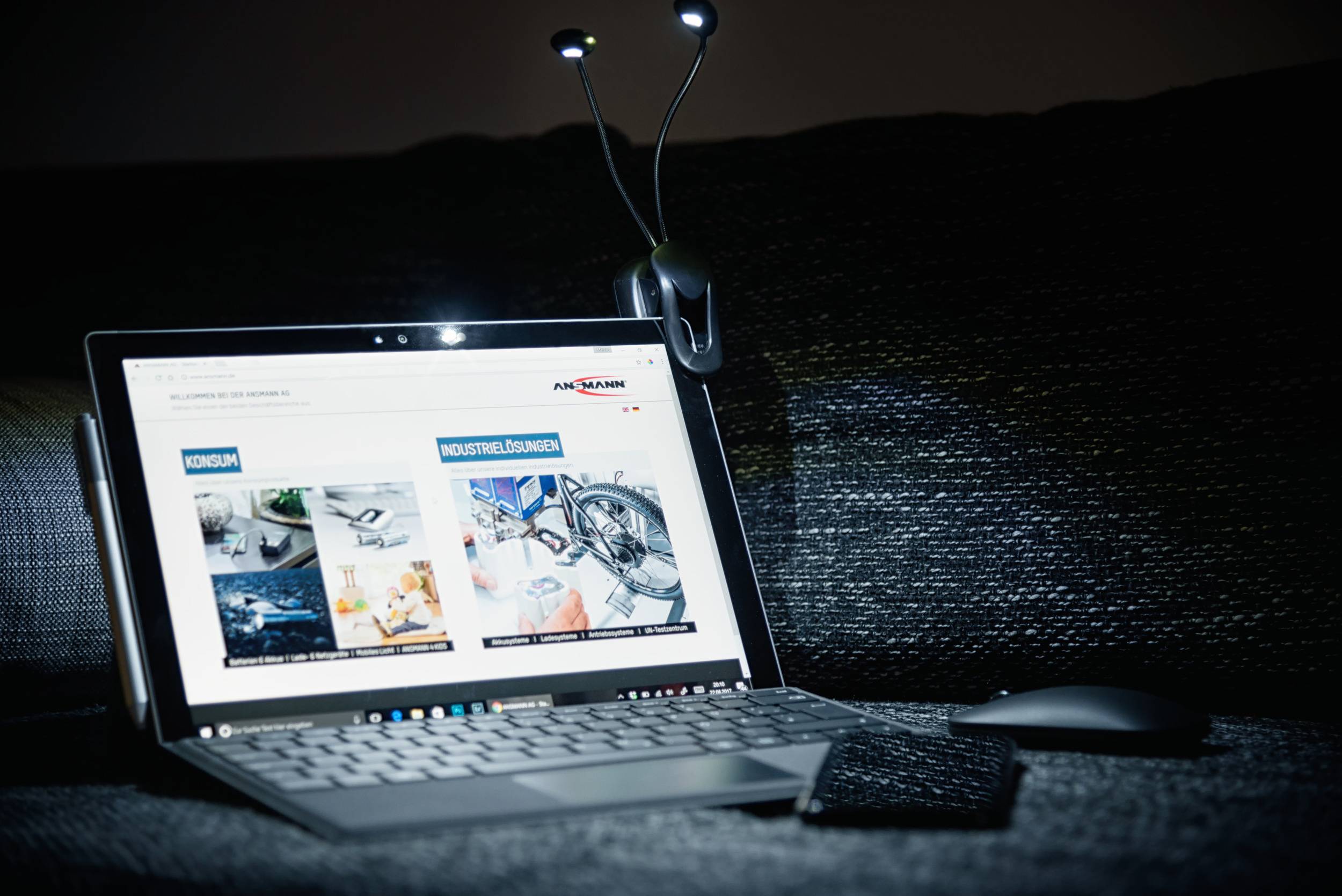 A laptop on a sofa displays a webpage with images of 'Cruise' and 'Industrial Solutions'. A lamp is visible in the background.