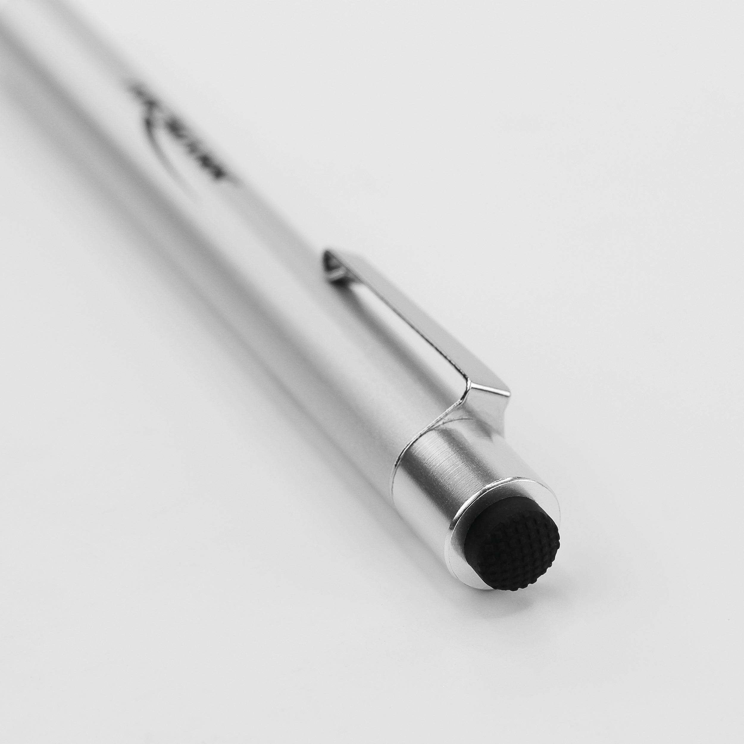 A silver ballpoint pen is lying on a white surface. The pen has a clip and a black tip.