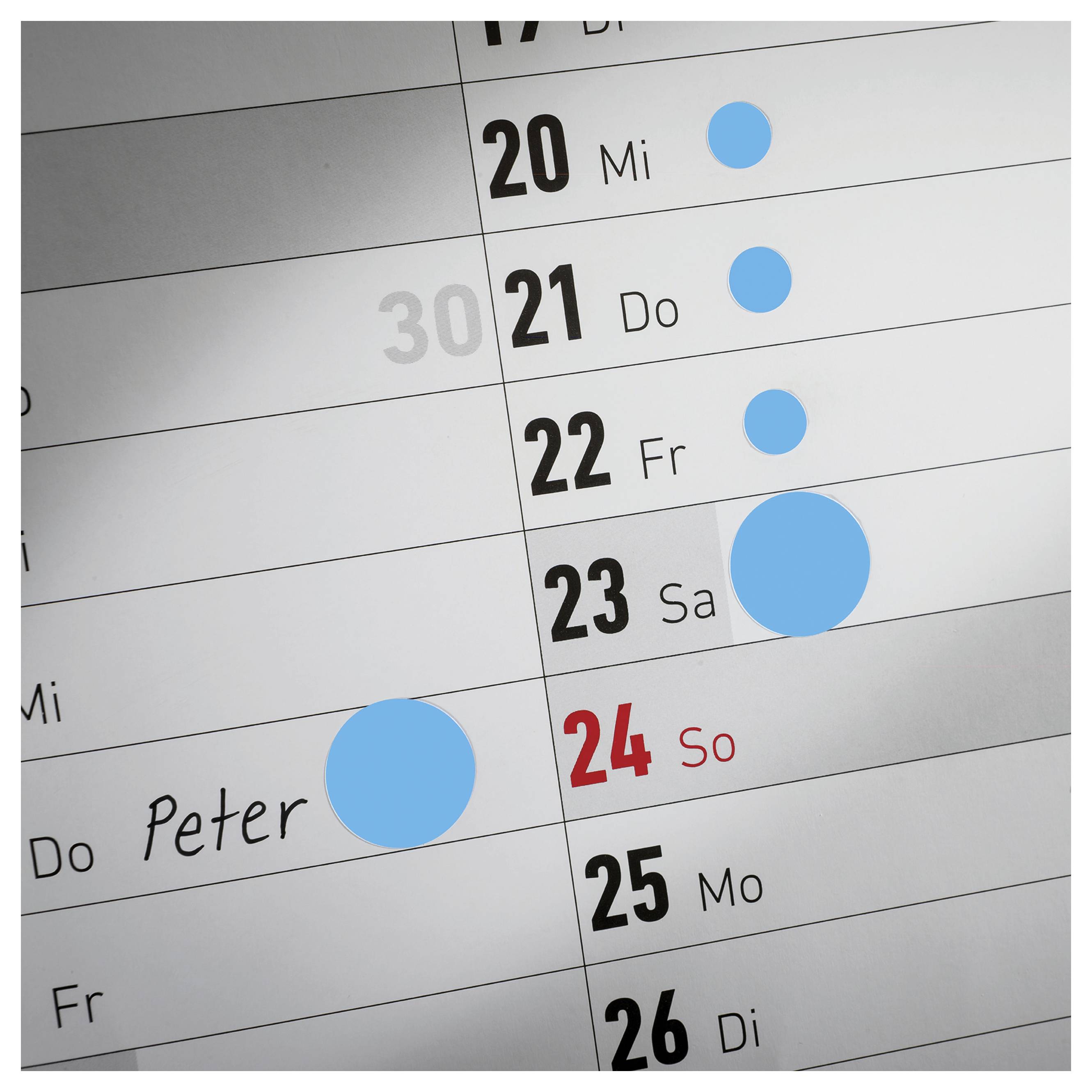 Close-up of a wall calendar with marked appointments: blue circles on 20th–23rd and 24th, name 'Peter' next to an appointment.