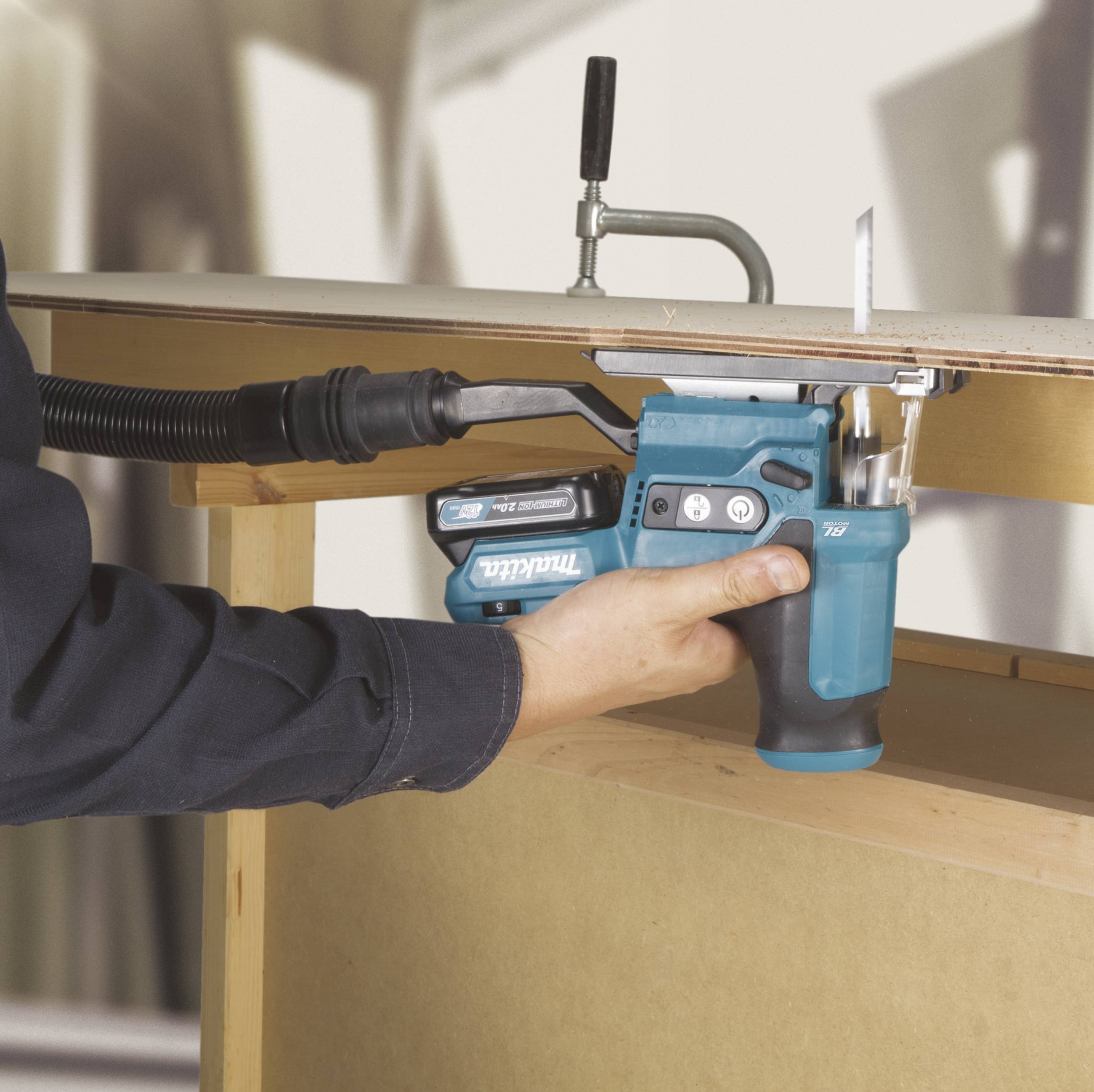 A person is using a blue cordless drill to drive a screw into a wooden board. The drill is secured to a workbench.