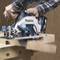 A person is using a blue and silver circular saw to cut a piece of wood. The saw is a 'Makita' brand.