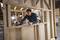 A person is working on a wooden frame in a workshop, using a tape measure and making markings on the wood for a precise cut.