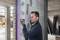 A man is using a laser distance measure to determine the width of a wall in an unfinished building.