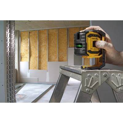 A hand is holding a laser level on a ladder in a room in a shell construction state; unfinished walls can be seen in the background.