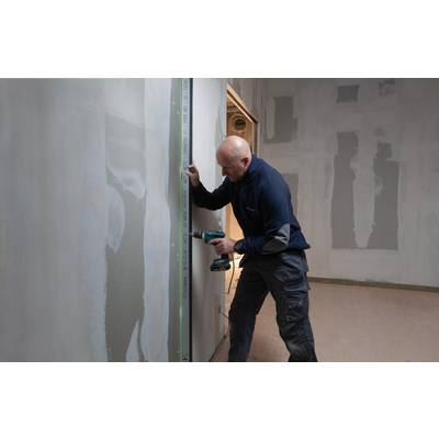 A tradesman is using a drill to secure a long ruler to a wall. The wall is partially plastered.