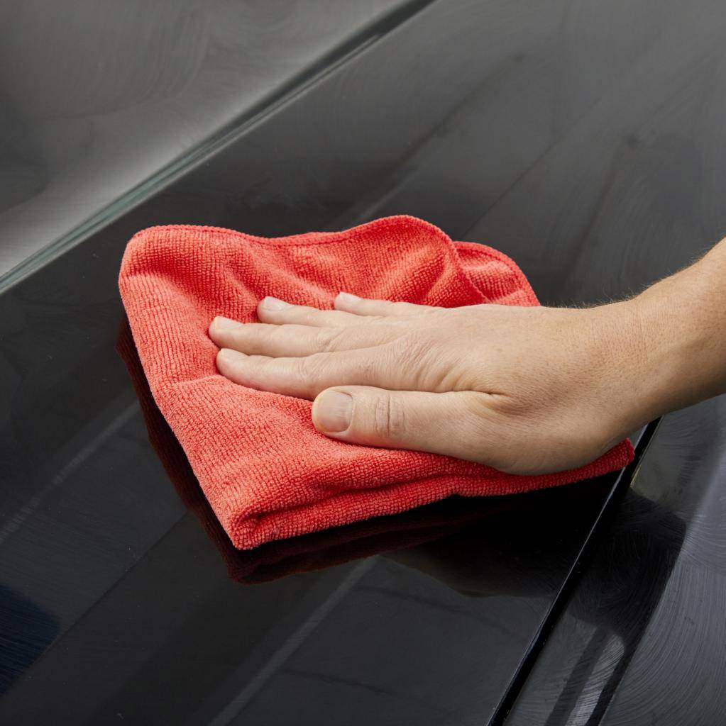 A hand wipes a red cloth over a shiny black surface, possibly for cleaning or polishing.