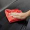A hand wipes a red cloth over a shiny black surface, possibly for cleaning or polishing.