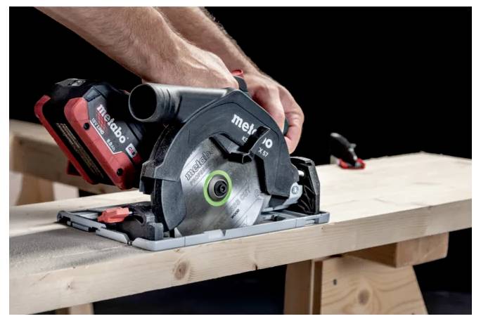 A person using a cordless circular saw to cut a wooden board on a workbench, focusing on precision and control.