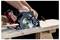 A person using a cordless circular saw to cut a wooden board on a workbench, focusing on precision and control.