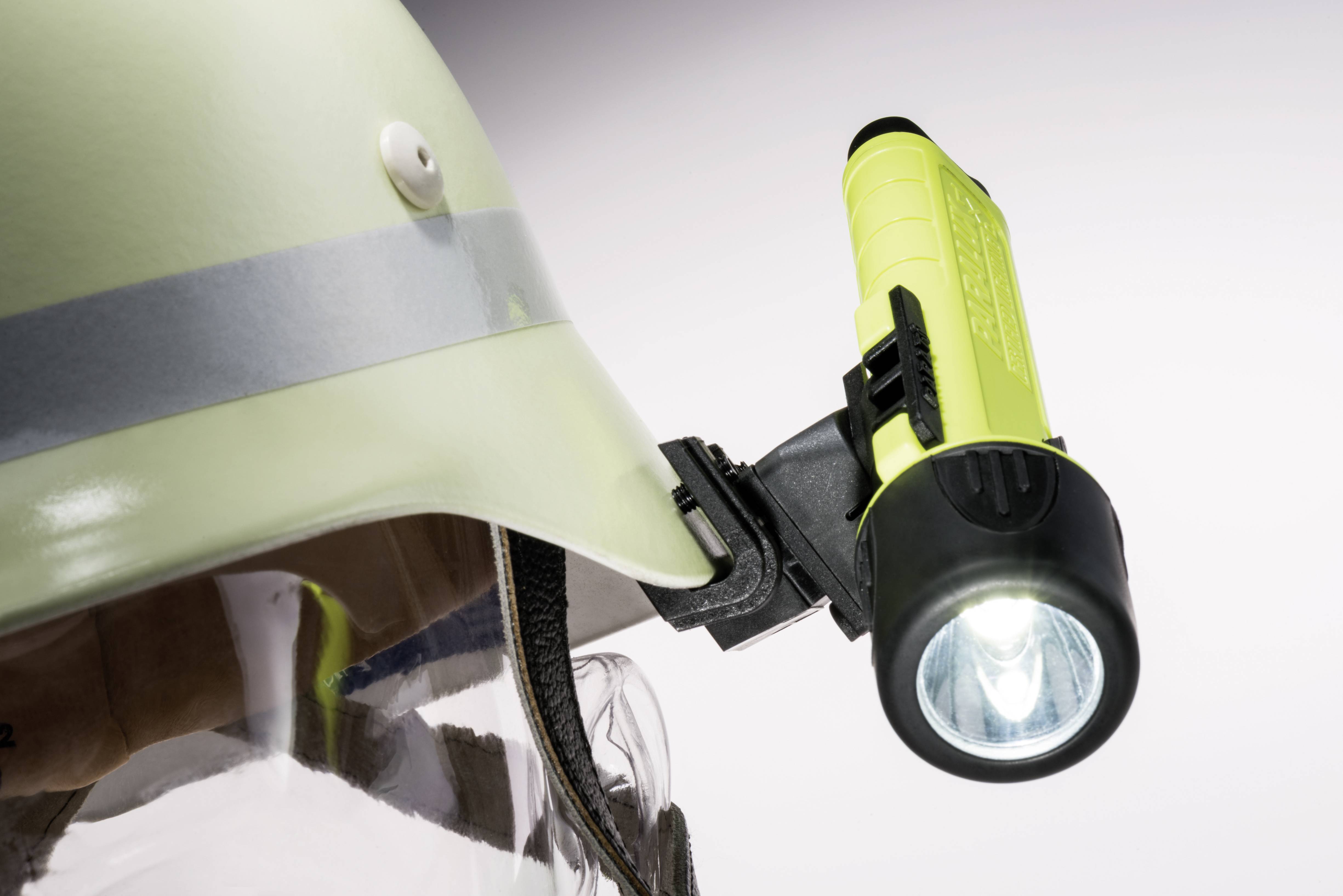 A safety helmet with a yellow torch attached to it, which is illuminated. The helmet has a transparent visor.