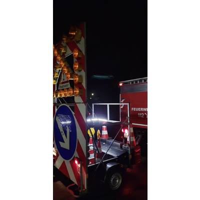 Fire engine on duty at night on the road. Warning signs and lights indicate a road closure. Traffic management is visible.