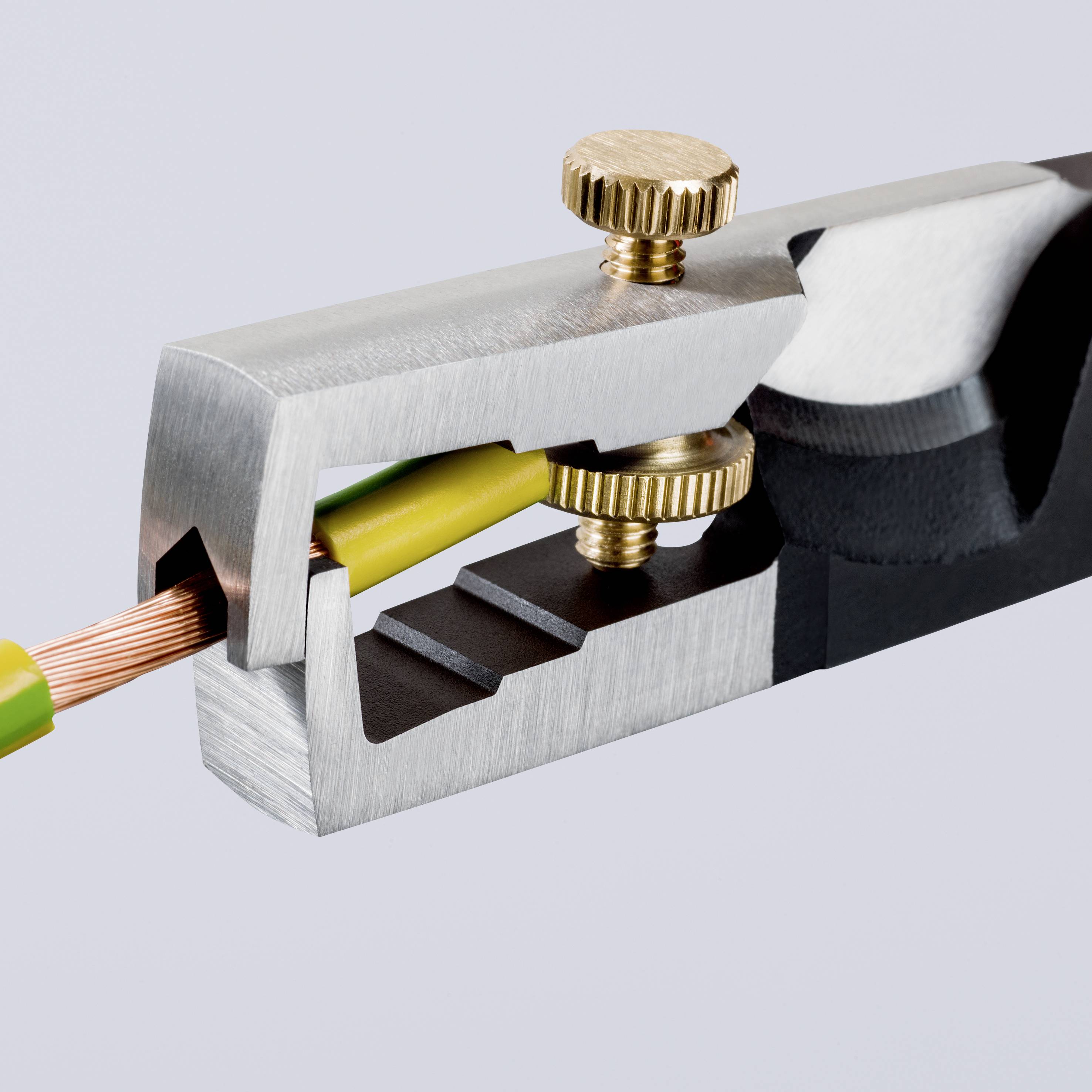 A silver cable cutter removes the insulation from a yellow-green cable made of copper.