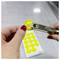 A person uses a hole puncher to mark a yellow circular sticker label, which lists numbers with a focus on the number '9'.