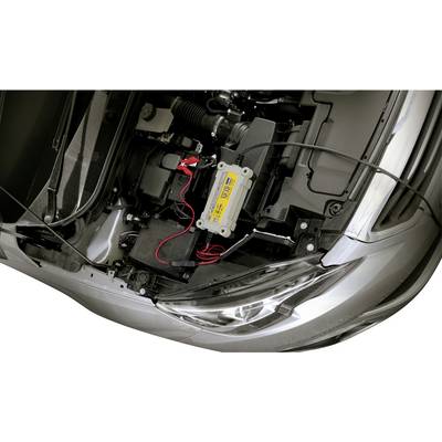 A car charger is charging a car battery in the open engine compartment of a vehicle. Red and black cables are connected.