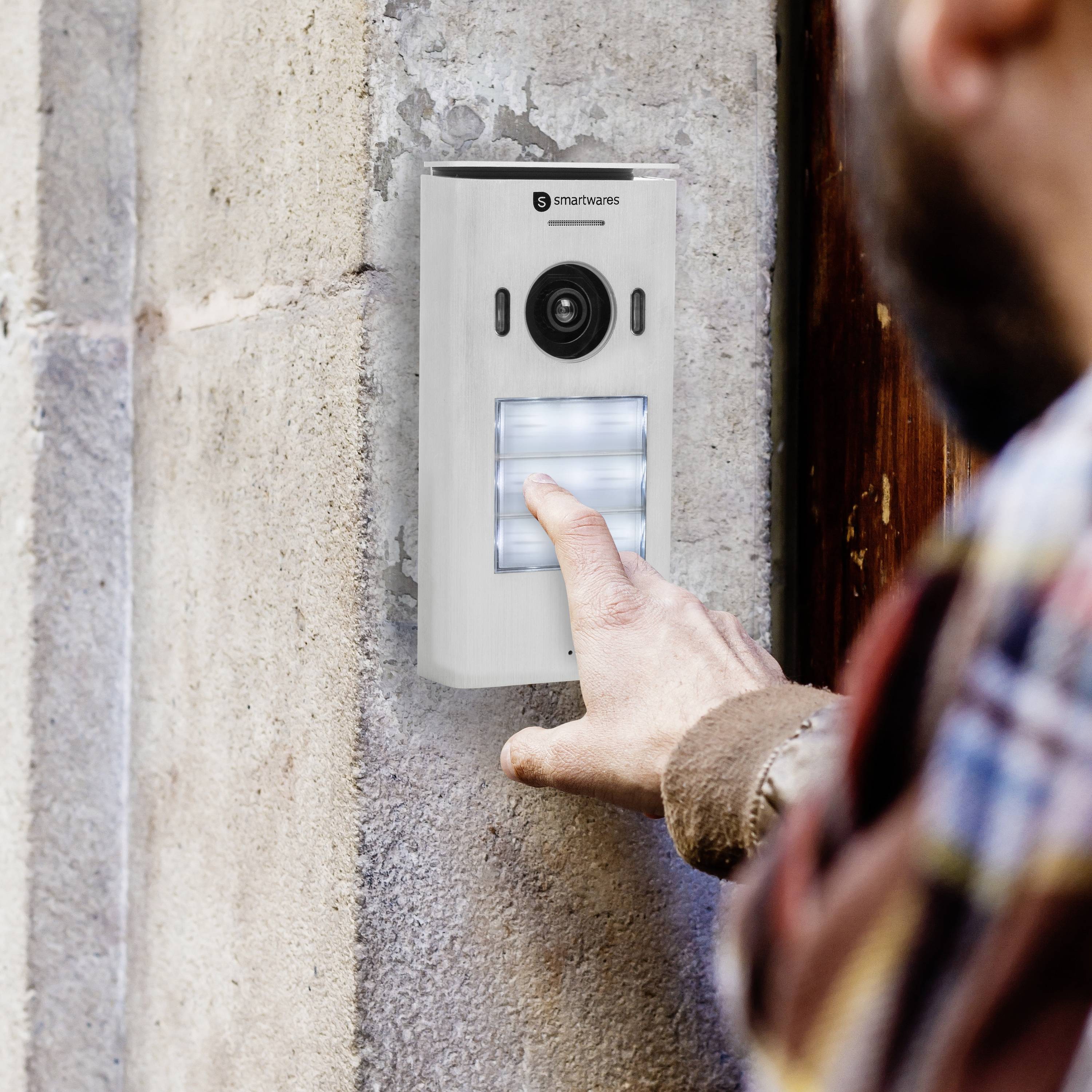 A person is pressing a modern video doorbell on a wall of a house.