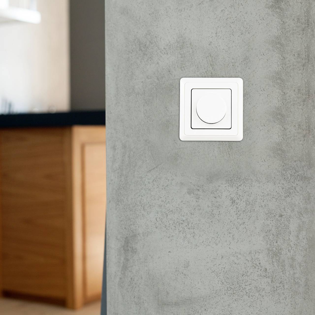 A white dimmer switch is installed on a gray wall inside a modern room, next to a wooden counter.