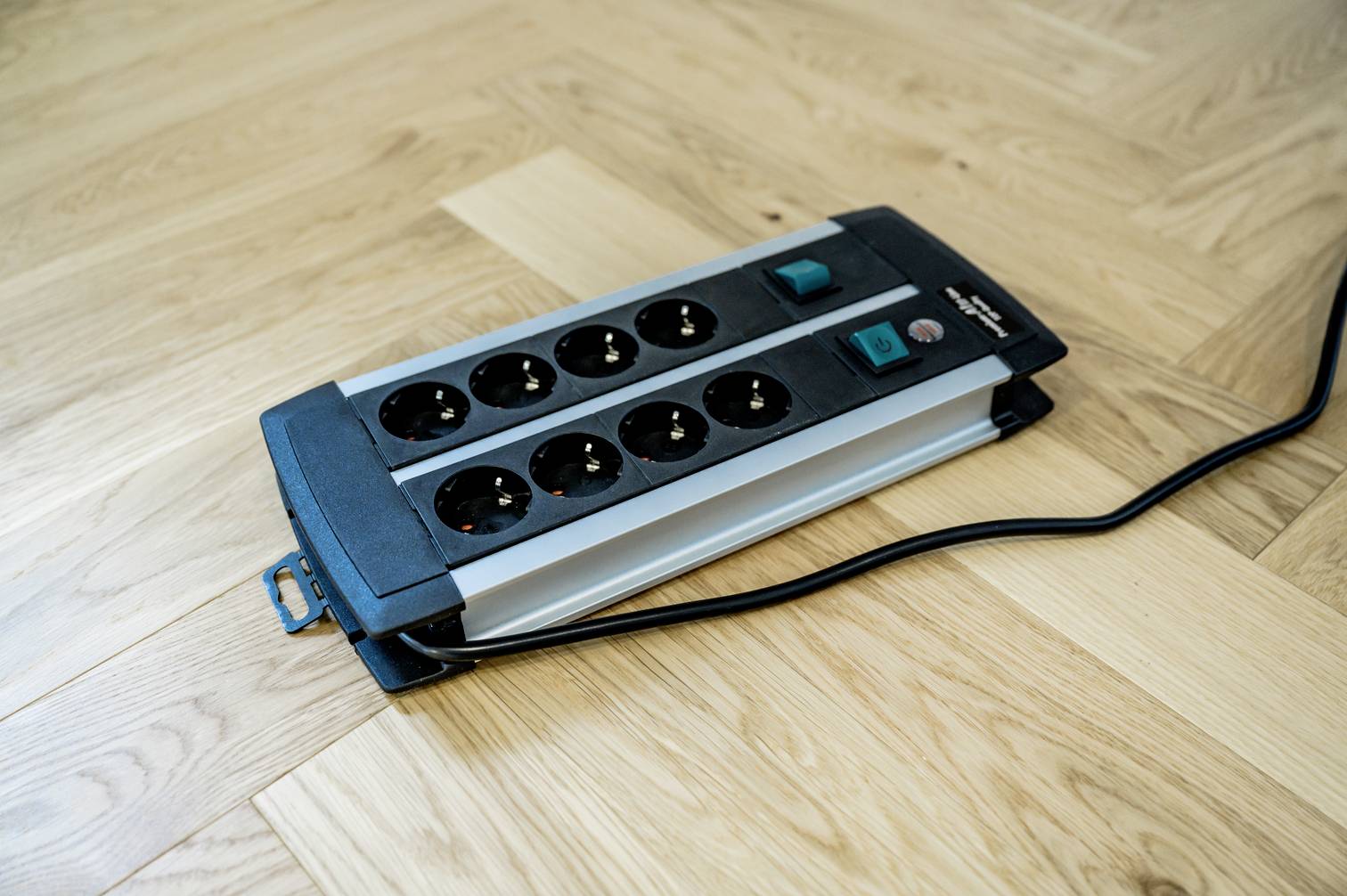 Eight-way power strip with two switches, placed on a wooden floor. One cable is connected.