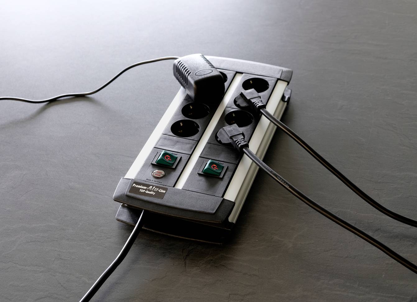 'Four-way extension socket with two sockets in use, featuring a switch for each row, placed on a grey surface.'