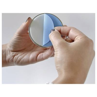 Hands hold a circular mirror while peeling away a blue protective film from its surface.