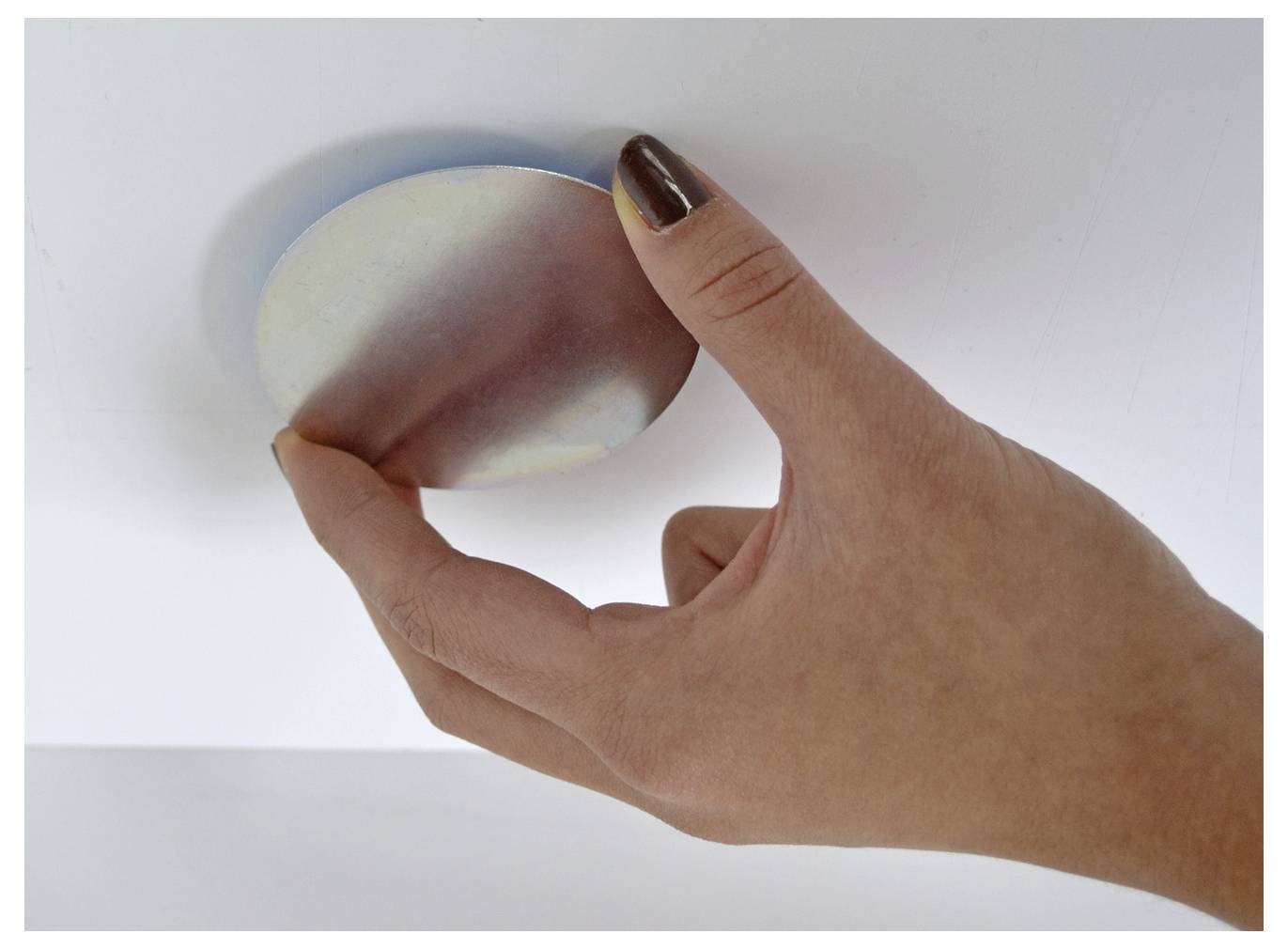 A hand presses a rounded white-and-pink stress ball against a white surface.