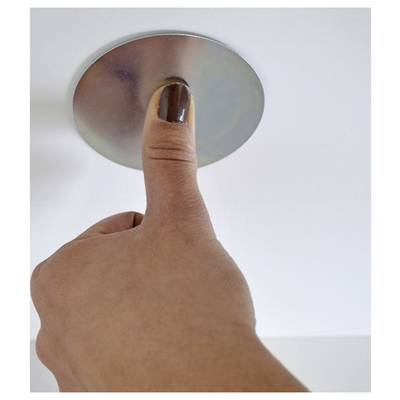 A hand with a painted thumbnail presses a round metallic button or ceiling fixture against a plain white background.