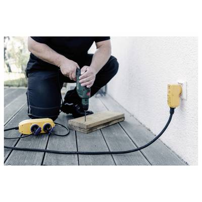 Person kneeling on a deck drills into a wooden board beside an outdoor electrical outlet with a plugged-in extension cord.
